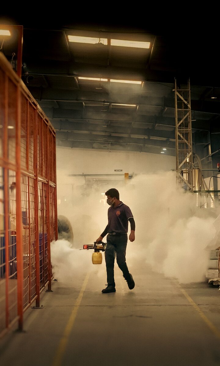 A worker in protective suit and respirator fogging the inside of a warehouse