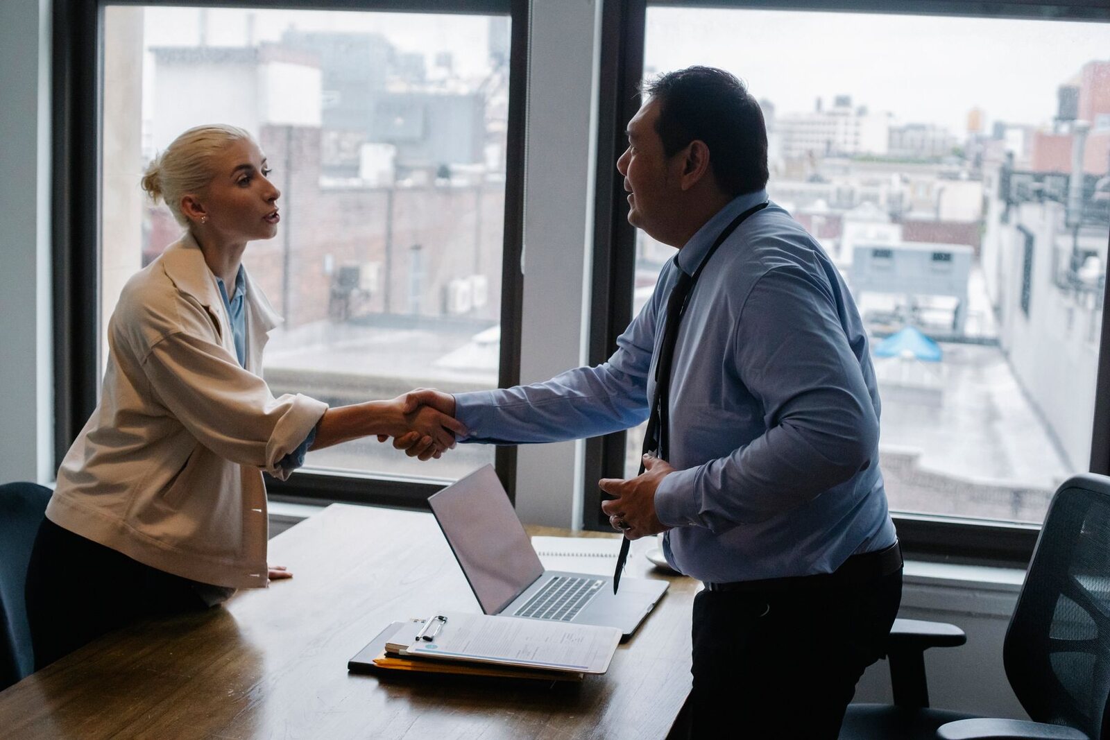 Two people shaking hands across a desk in an office interview