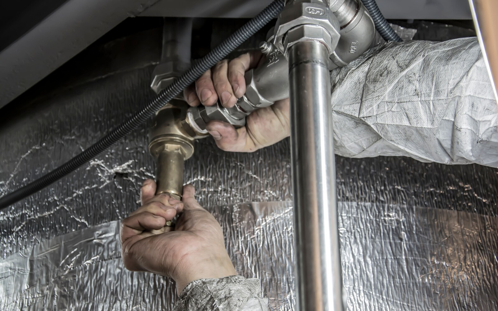 An engineer working on metal pipework beside insulated plant equipment