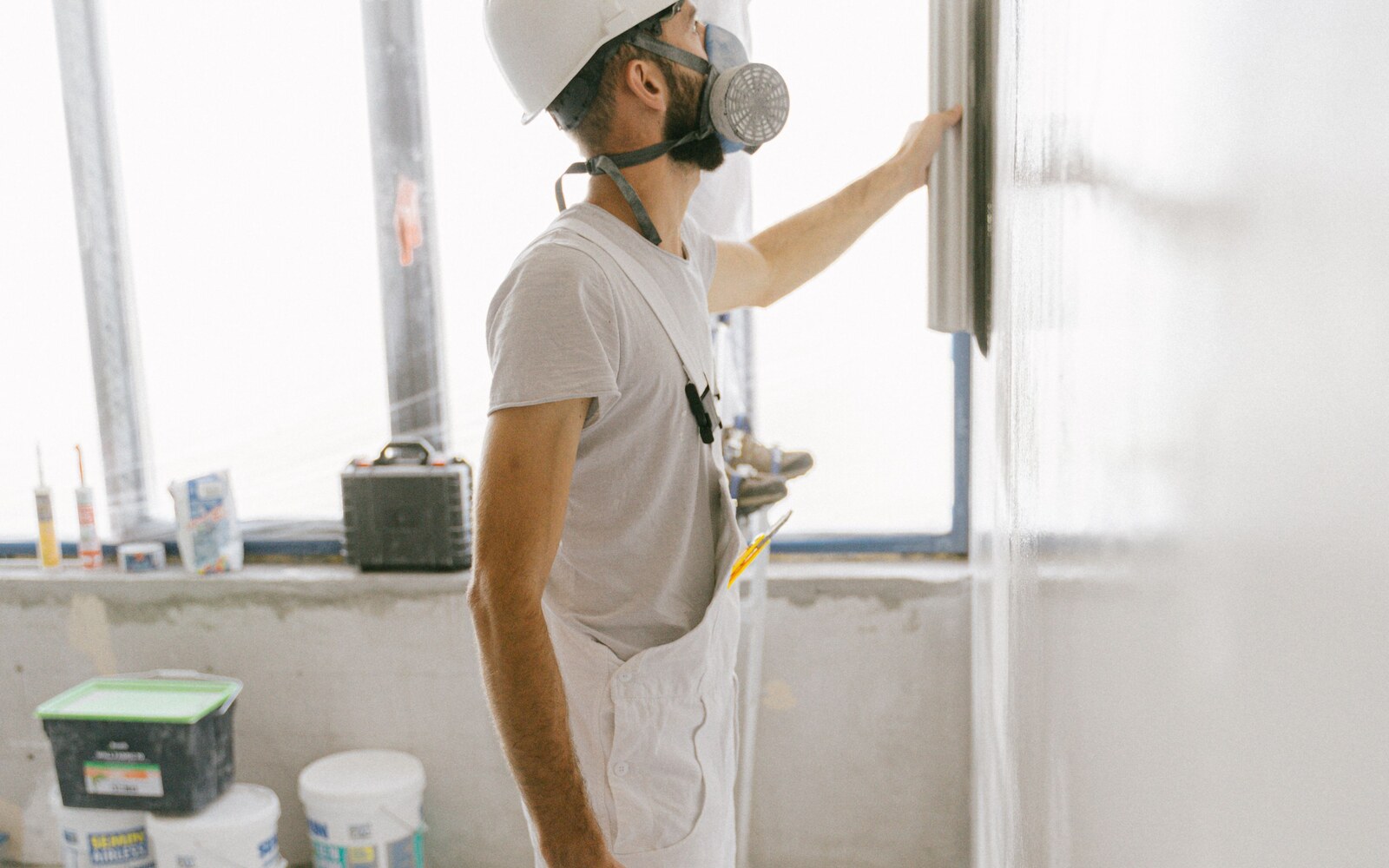 A renovation worker wearing a dust mask and smoothing plaster on an interior wall