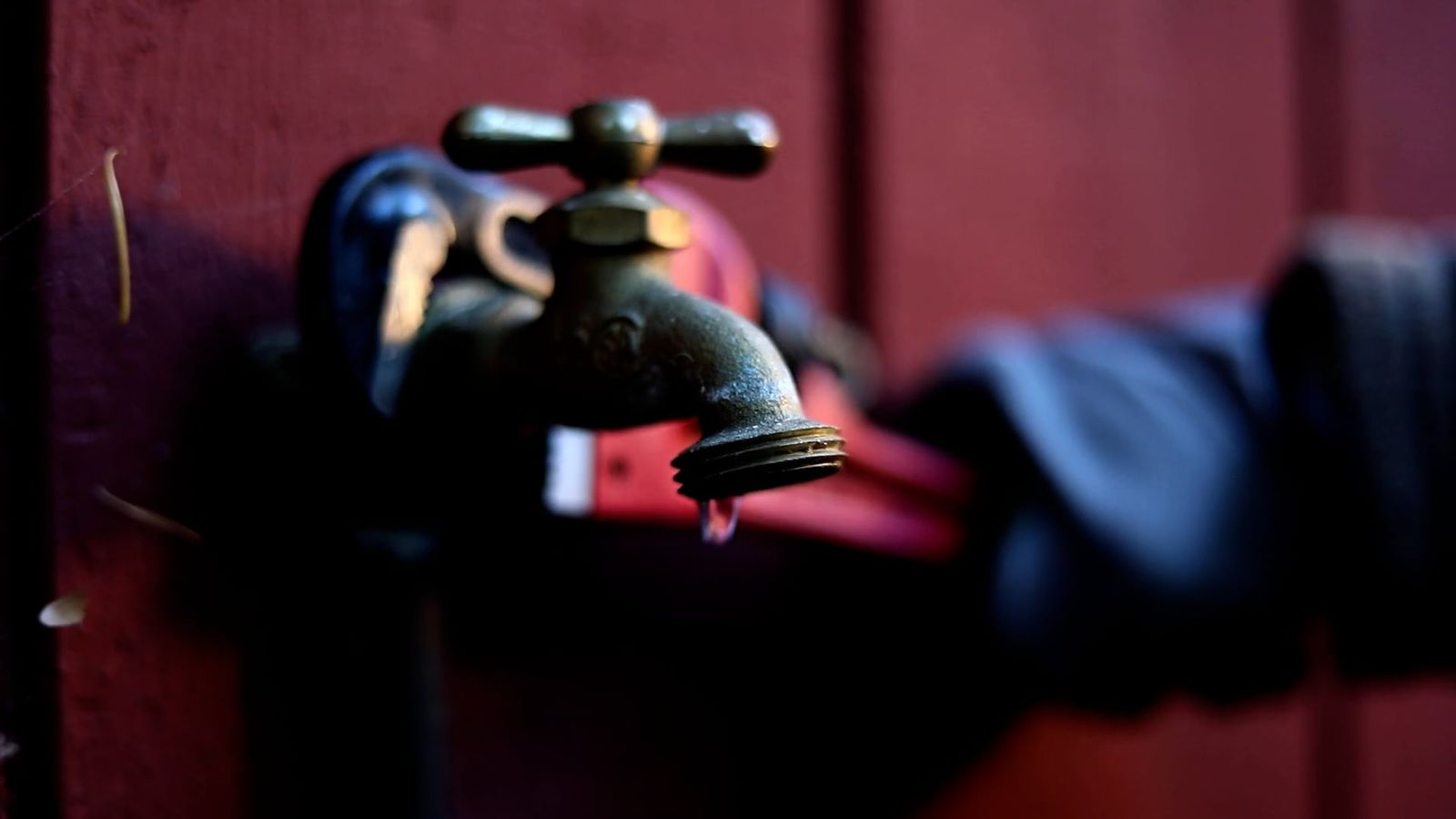 Close-up of a gloved hand beside a brass outdoor tap with a drip forming at the spout
