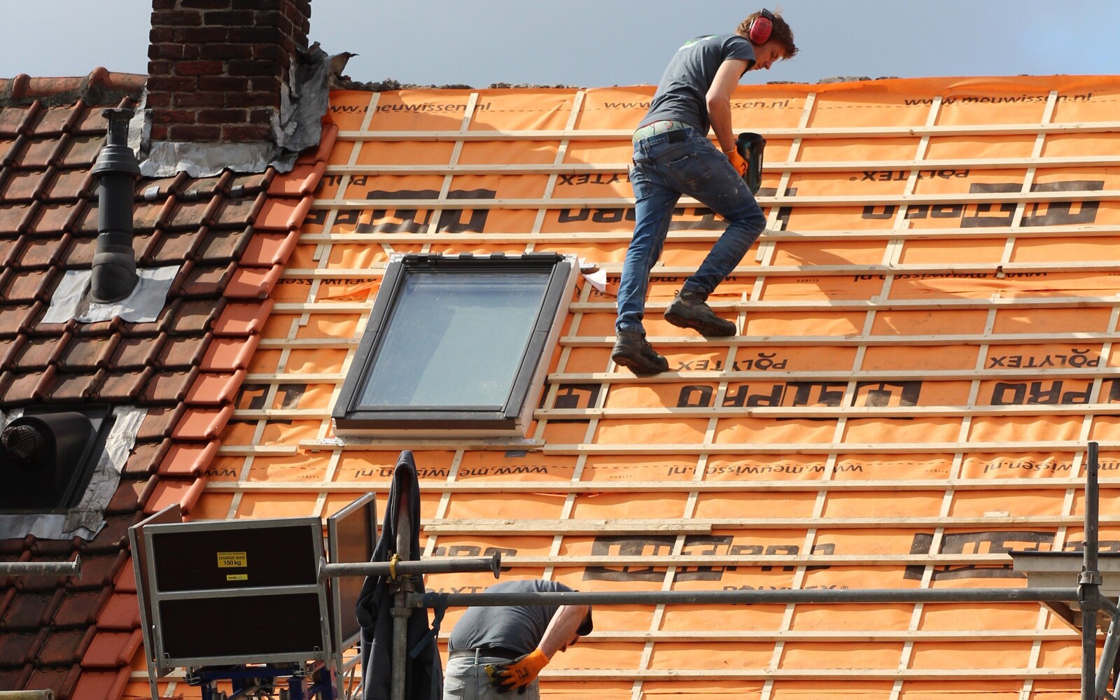 Workers fitting roof battens and tiles around a skylight on a pitched roof